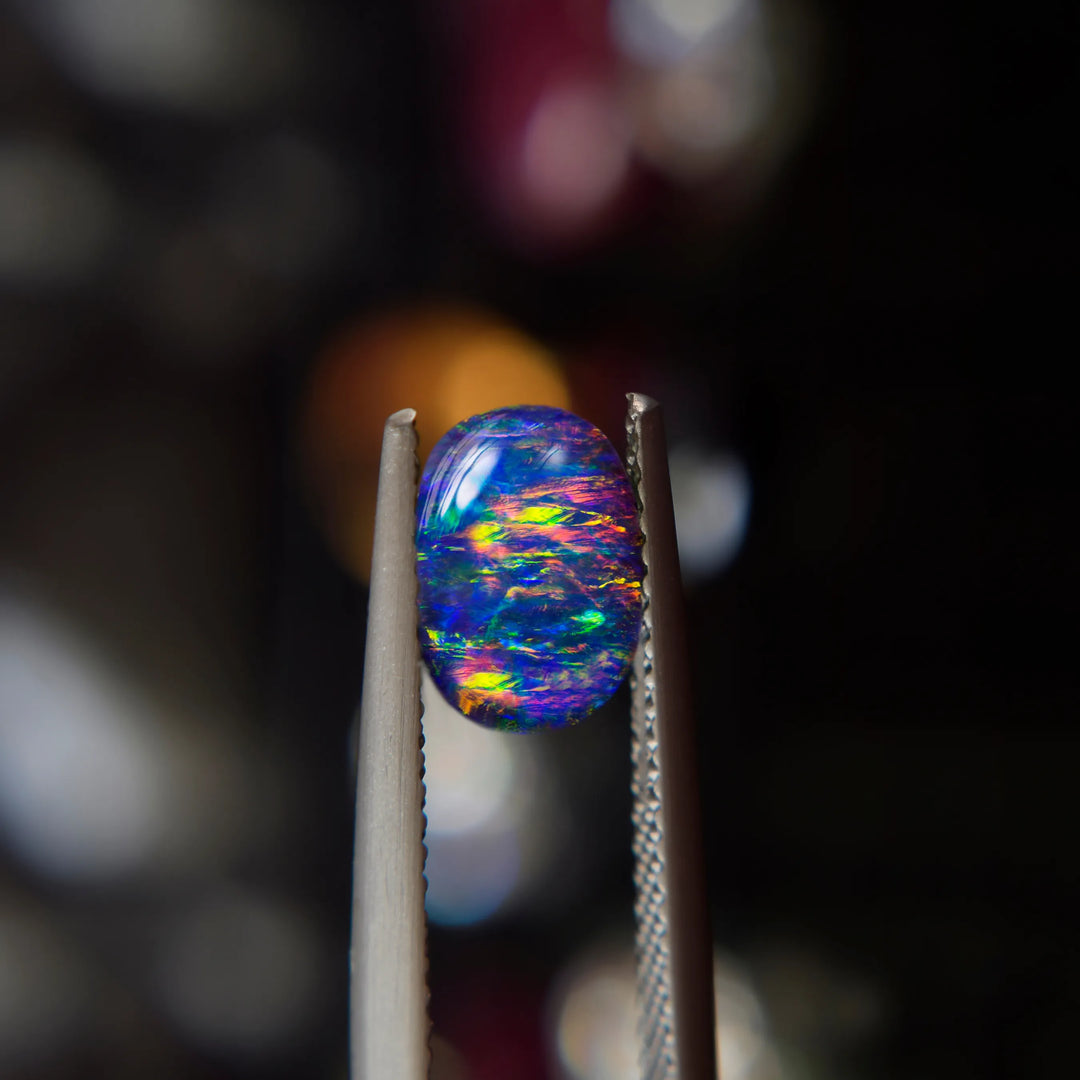 An oval cabochon black opal held between jeweler's tweezers