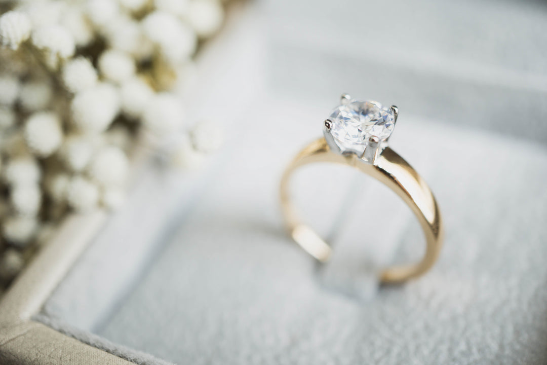 Gold ring with a diamond on a soft surface with blurred flowers in the background