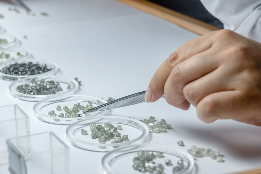 A professional jewelers sorts through raw diamonds using a tweezer.