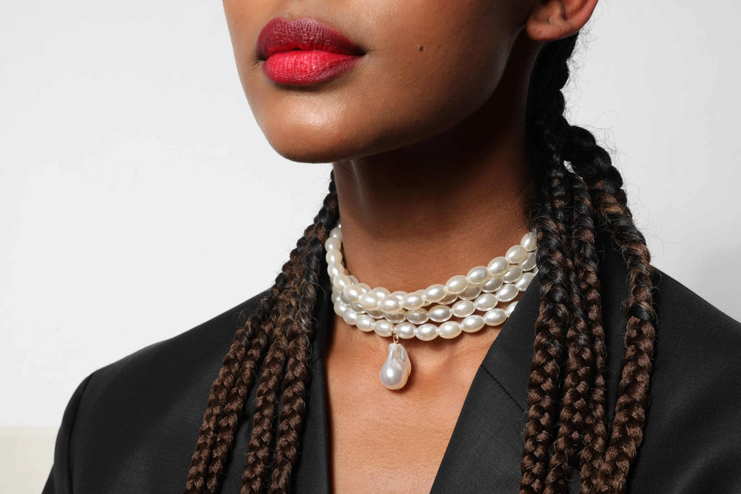 Woman wearing a pearl necklace with braided hair against a neutral background