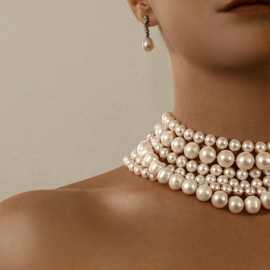 Close-up of a person wearing multiple pearl necklaces and earrings against a neutral background