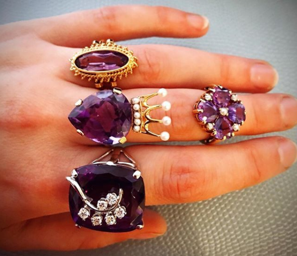 A model's hand wearing a variety of antique estate rings with amethysts, pearls, and diamonds
