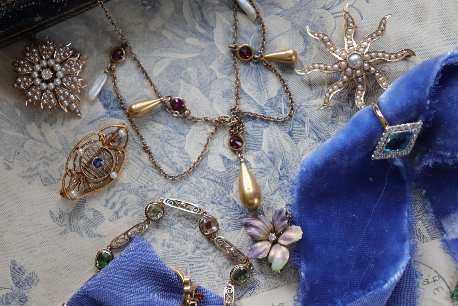 A styled flat-lay of vintage jewelry, including brooches, a ring, a bracelet, and a necklace set with gemstones, diamonds, and pearls.