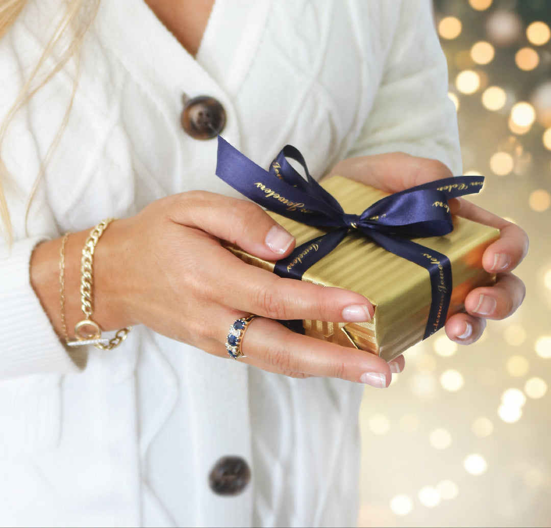 Person holding a gold gift box with a blue ribbon against a festive background