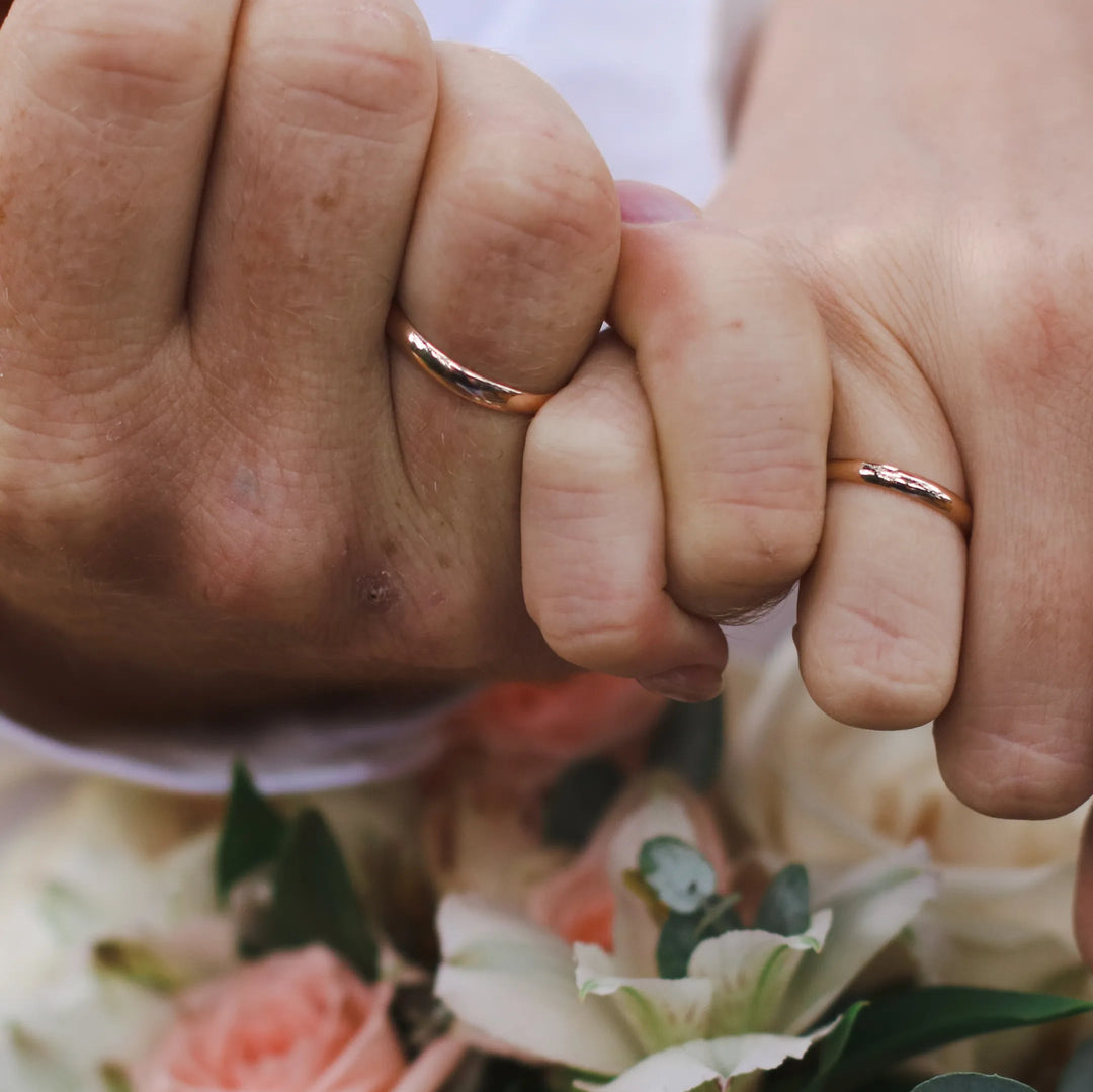 Two hands in a pinky promise gesture with both wearing wedding bands