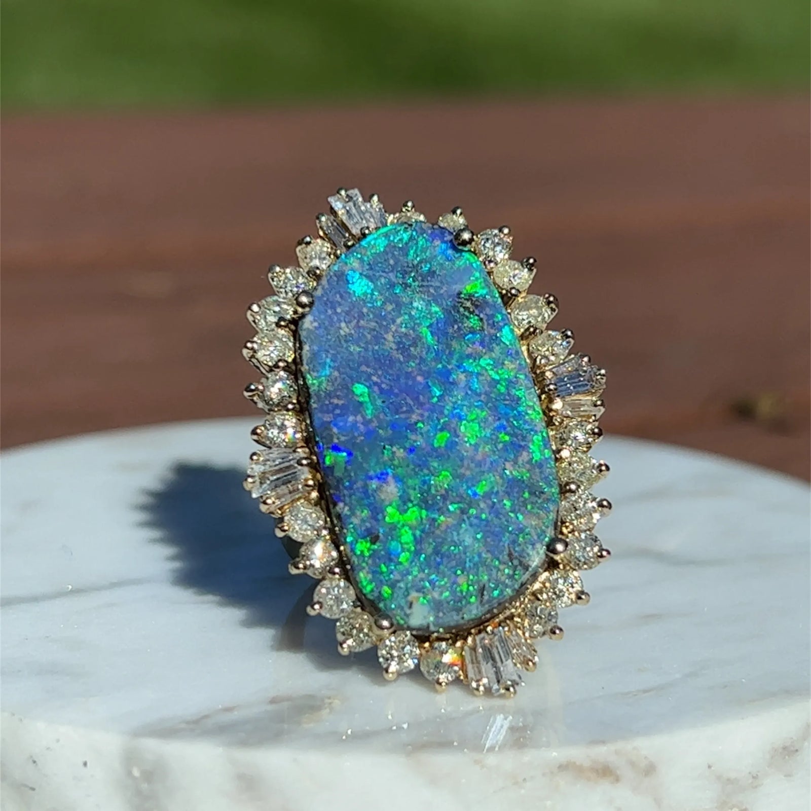 Ring with a large black opal stone and multi-shaped diamond halo on a marble surface.
