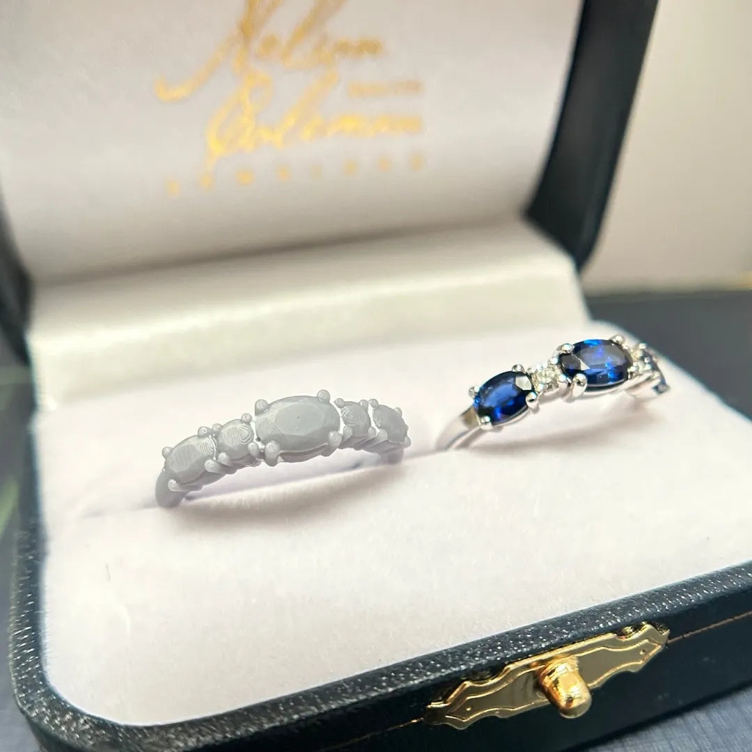 A wax model next to the finished product of a blue sapphire and diamond band inside of a Nelson Coleman Jewelers jewelry box