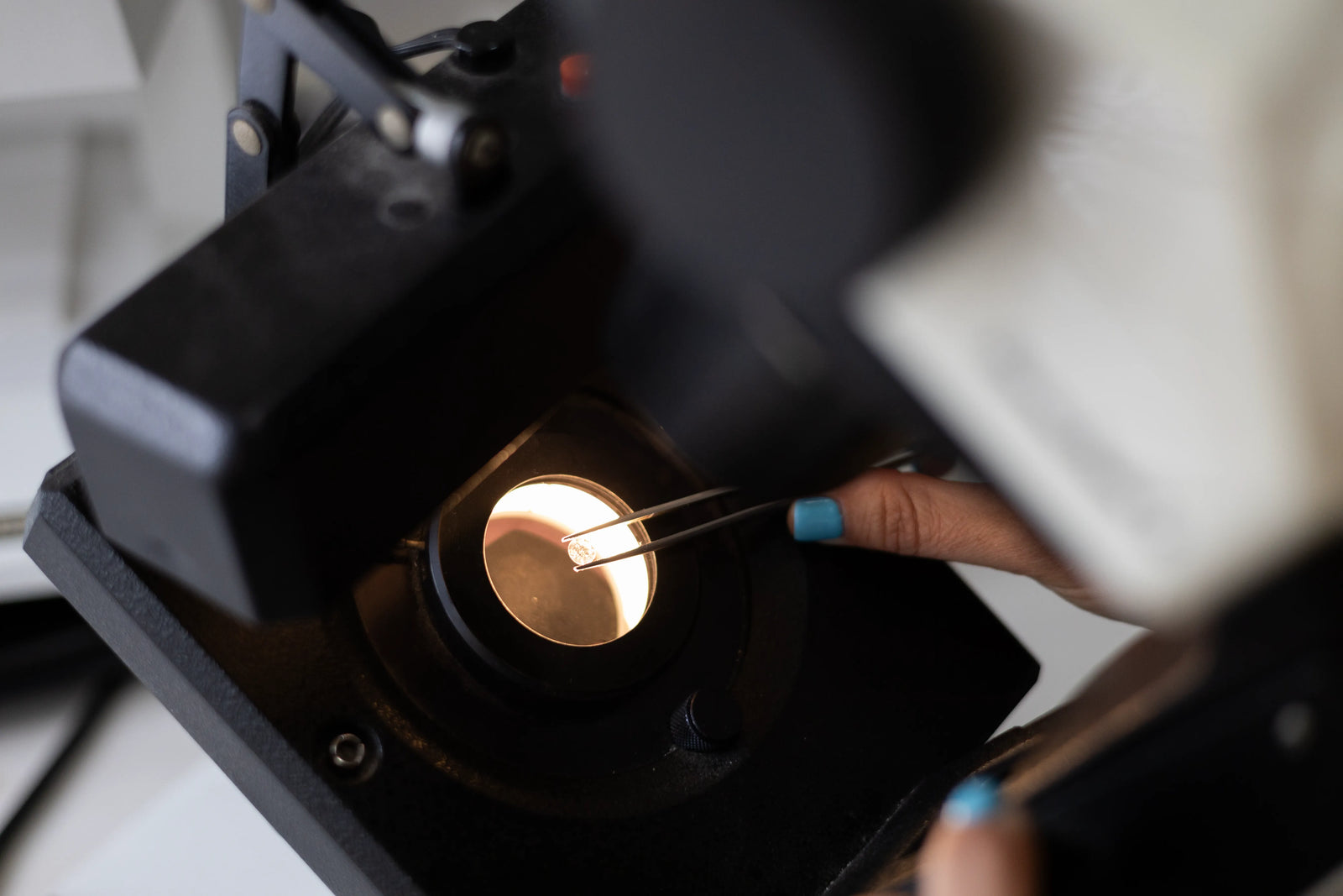 A close-up shot of a professional jewelry appraiser using tweezers to place a loose round brilliant-cut diamond on a magnifying lamp stage.