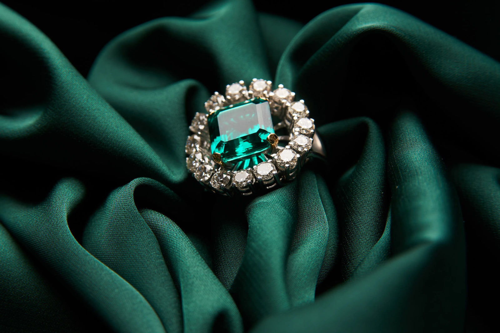 An emerald-cut emerald and diamond ring resting on green silk fabric
