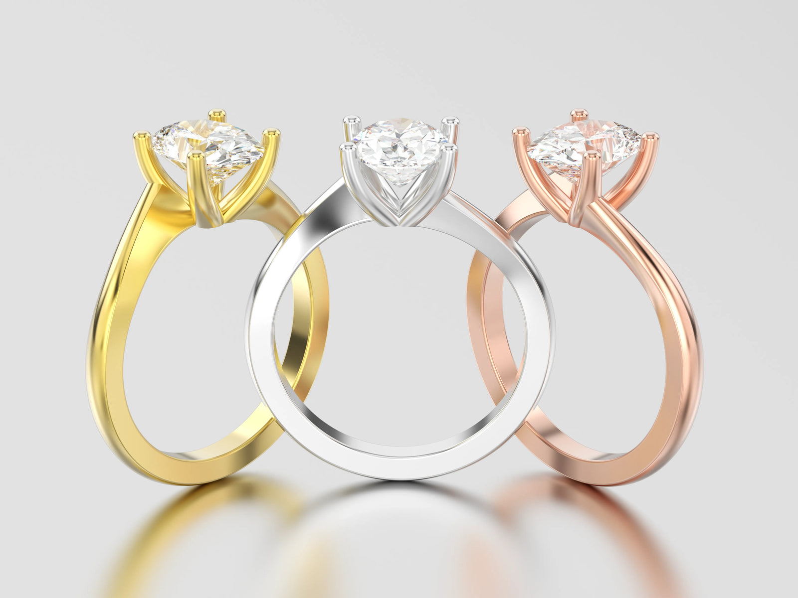 Three diamond solitaire engagement rings each in a different metal color option including yellow gold, white gold or platinum, and rose gold on a grey reflective background