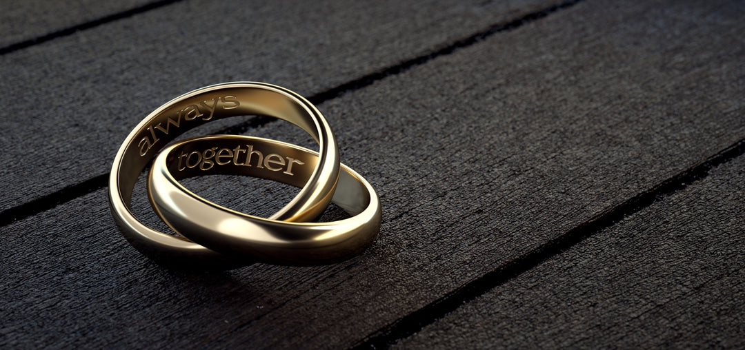Two interlocking gold rings with 'always together' engraving on a dark wooden surface