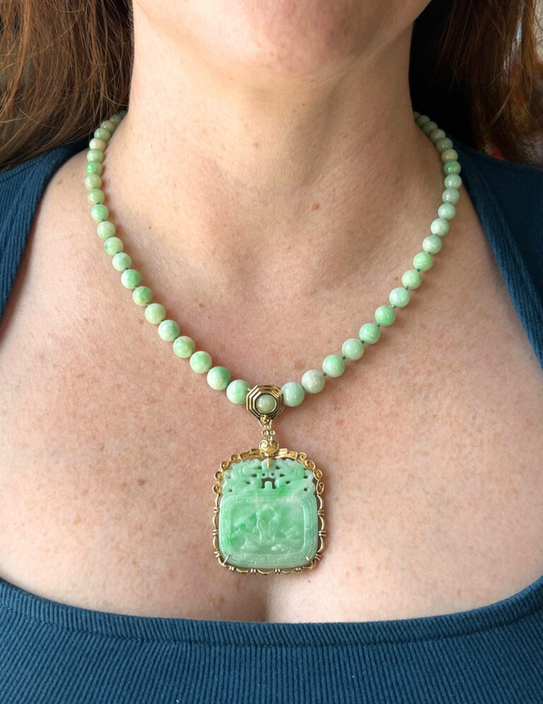 An estate gold and jade pendant necklace being worn by a woman with light brown hair and a blue shirt