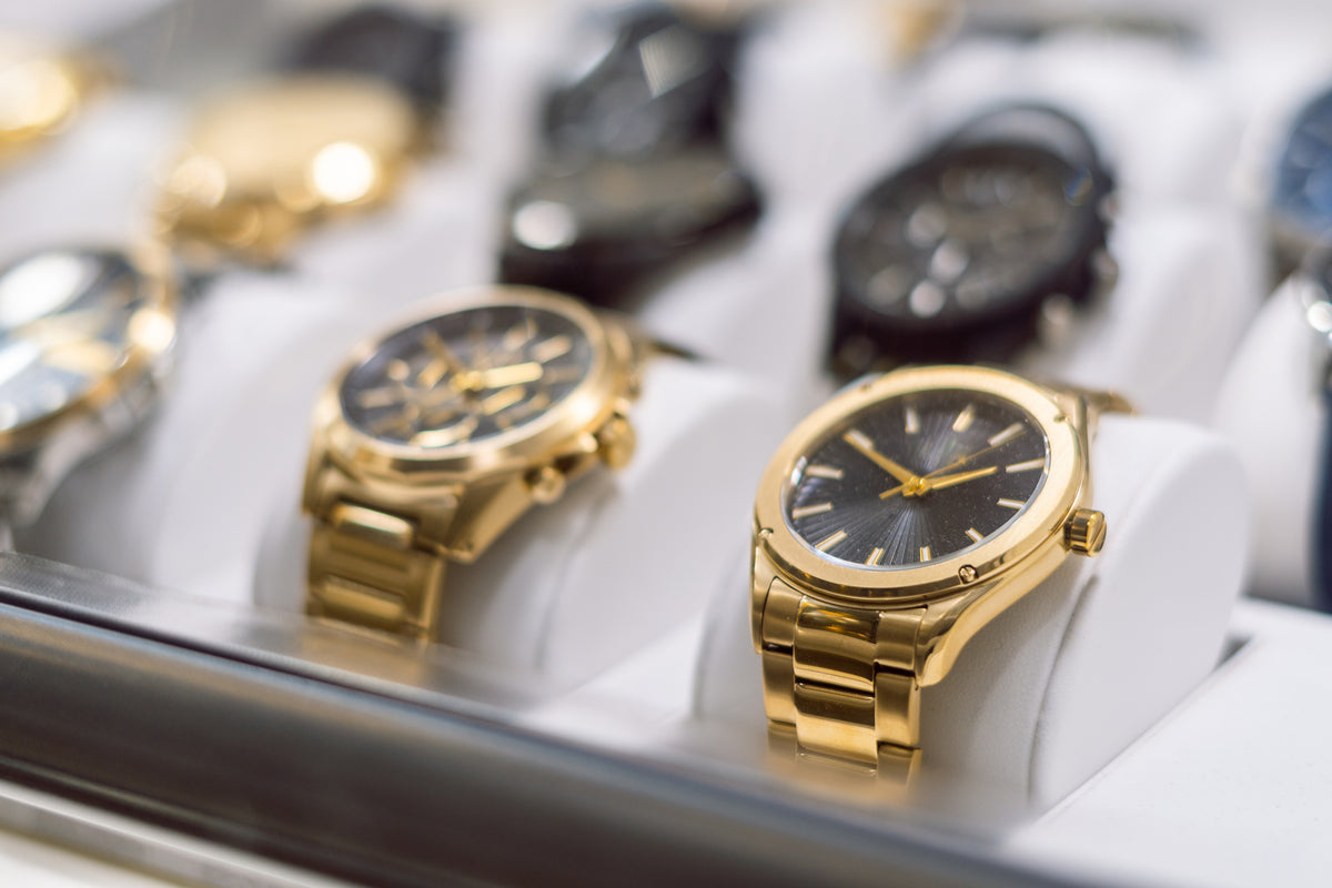 A collection of luxury watches in a case including gold-tone watches in the front with a blurred background.