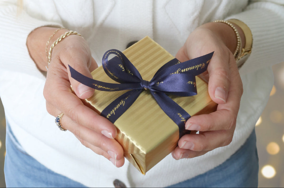 Person holding a gold gift box with a blue ribbon