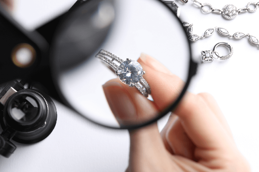 A close-up image of a professional jewelry appraisal of a diamond engagement ring being held by a woman's hand under a magnifying glass.