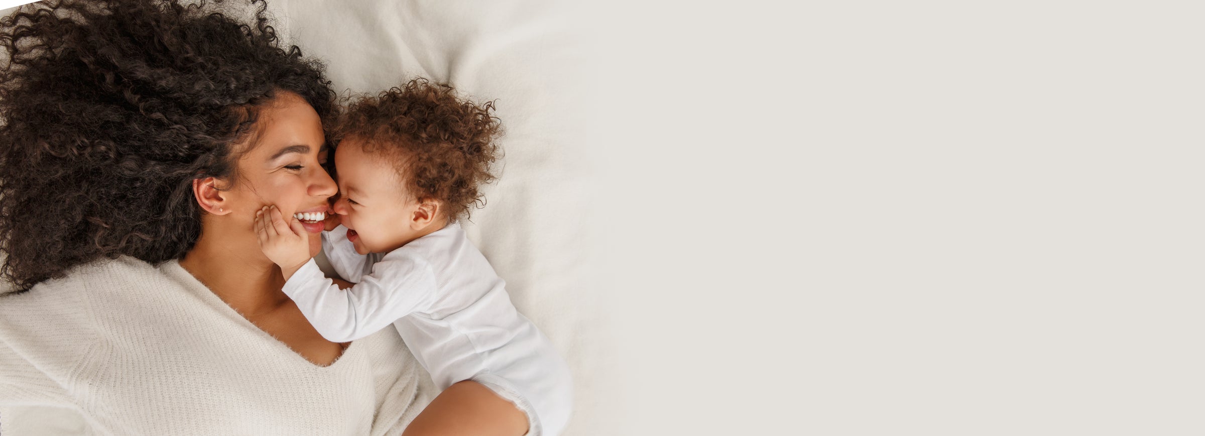 Woman and child lying on a white bed, smiling and laughing.