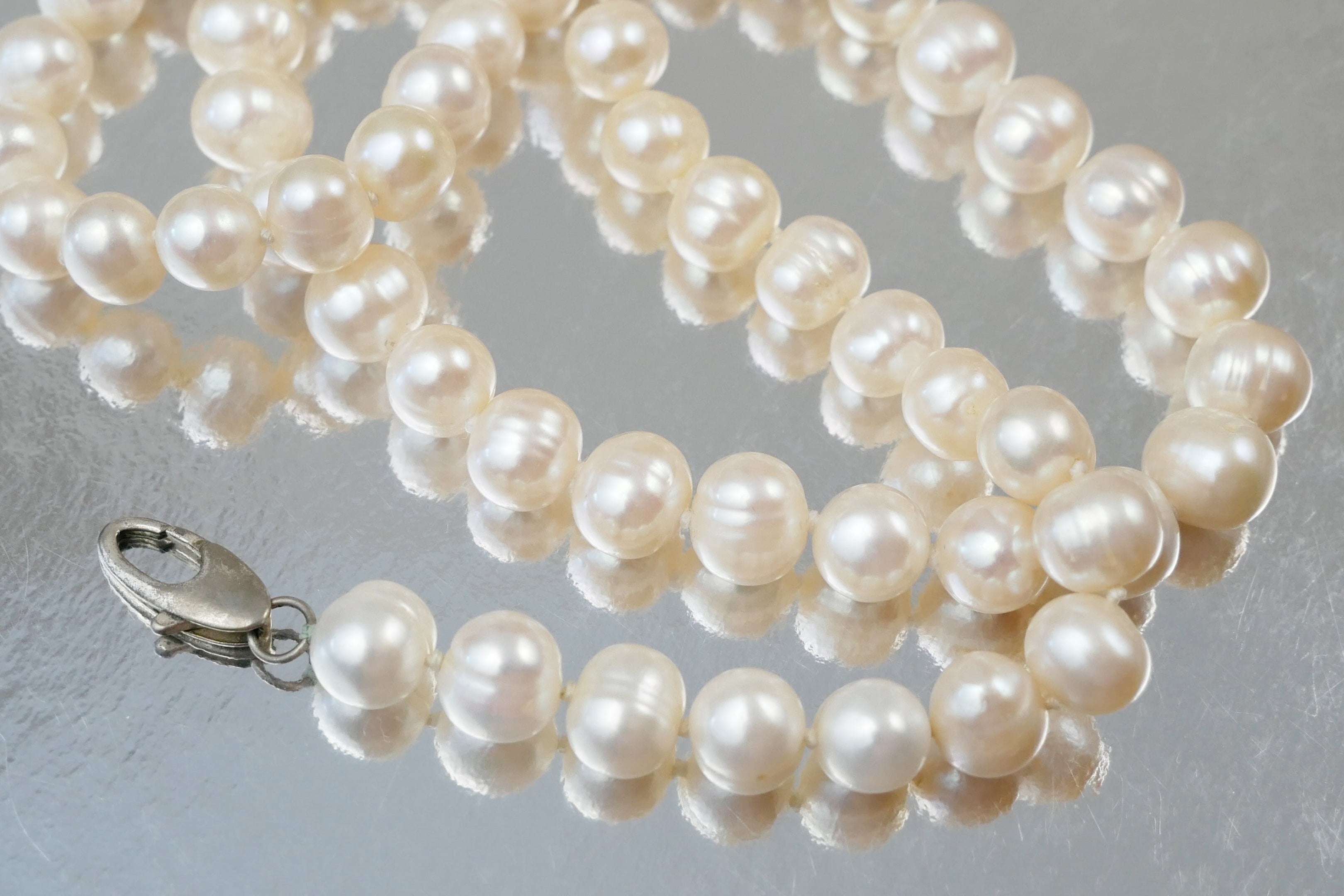 Pearl necklace with a silver clasp on a light gray background
