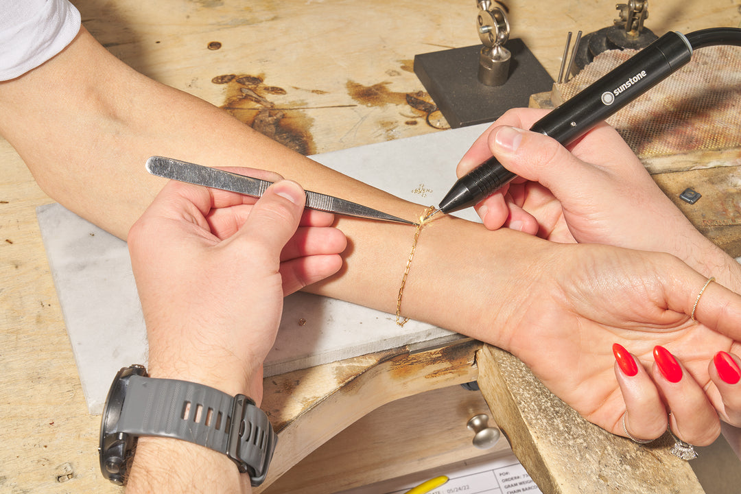 A close-up of a person attaching a permanent jewelry bracelet