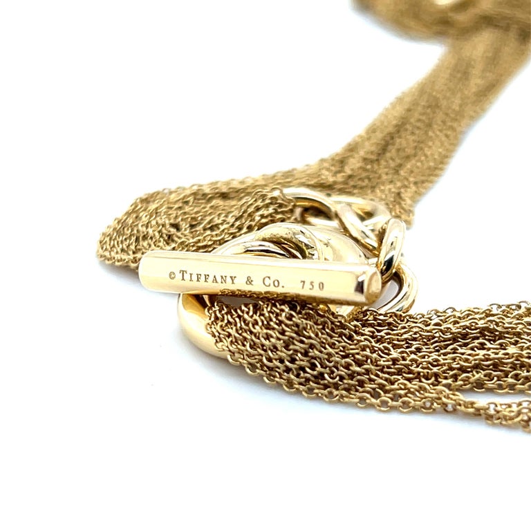 Close-up of a gold chain necklace with a toggle clasp engraved with '©Tiffany & Co. 750', on a white background.