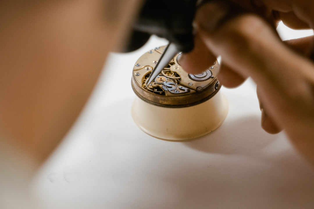A close-up shot of a watchmaker's hands using a precision tool to adjust the internal gears of a vintage-style watch inside a magnifying loupe.