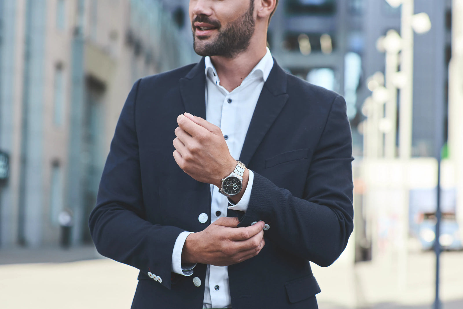 Man in luxury watch and suit adjusting blazer outdoors with blurred background