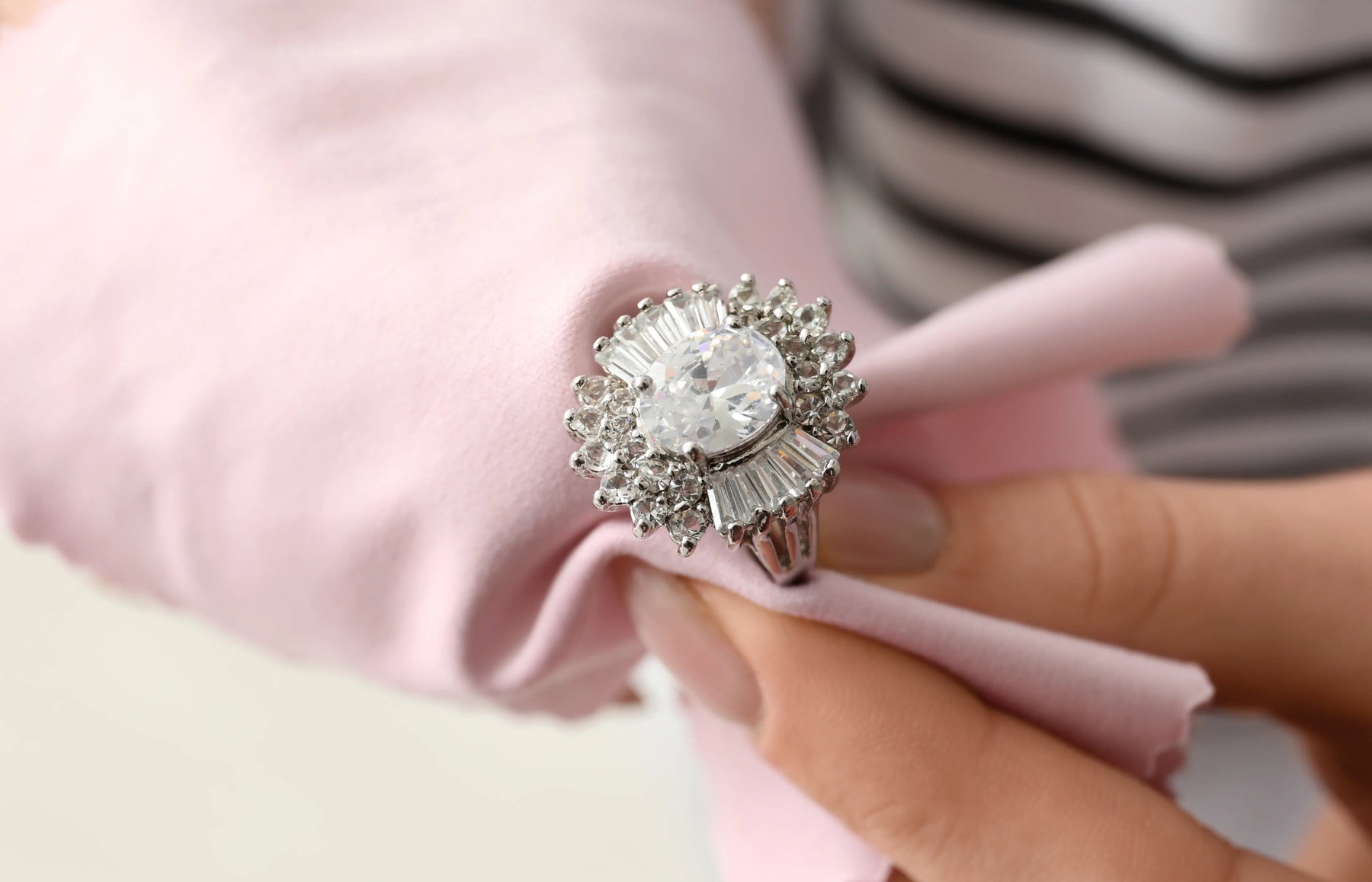 A close-up of an estate diamond ring being cleaned by a woman using a soft pink cloth.