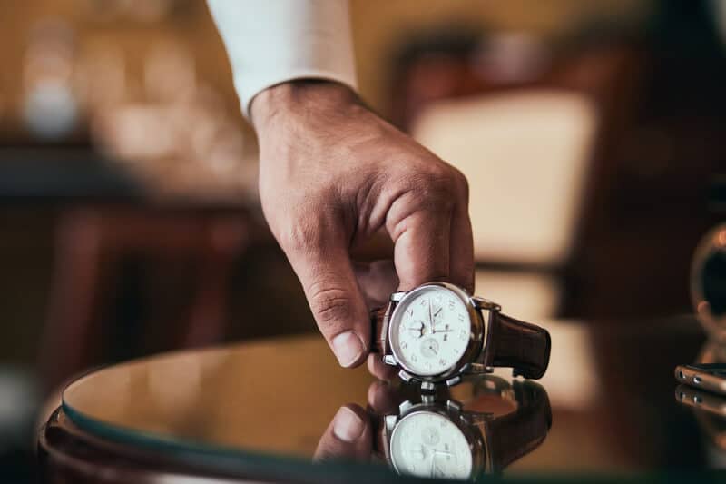 A man’s hand places a fine watch on a lacquered table surface.