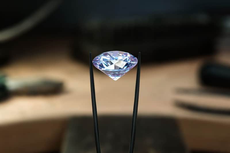 A diamond is centered in the frame, held up with slim tweezers.