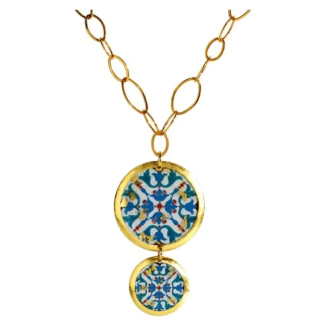 22 karat yellow gold leaf finish double-sided pendant necklace by Evocatuer featuring images of patterns found in the city of Pompeii. The pendant features a 1.5" disc with a short drop to a 1" disc . The pendant is attached to a 30" long oval link chain.