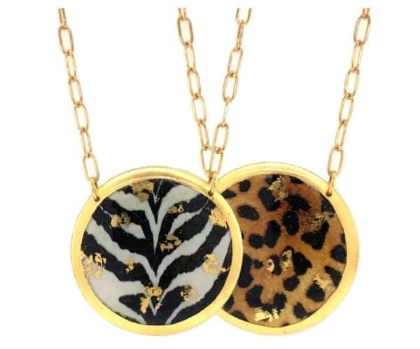 One 22 karat yellow gold leaf finish double-sided pendant necklace by Evocateur featuring a round disc pendant with a zebra pattern on one side and a leopard pattern on the other side. The pendant measures 1.5". The length of the necklace is 17".