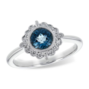 One 14 karat white gold vintage-inspired London blue topaz and diamond halo ring containing a round checkerboard-faceted London blue topaz weighing 0.93 carats in a milgrain-accented bezel setting and a fancy shaped halo with milgrain accents containing round brilliant diamonds. By designer Allison Kauffman.