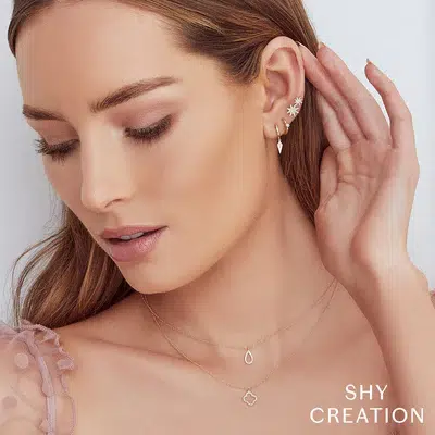 a model wearing a 14 karat yellow gold clover-shaped pendant necklace by Shy Creation with 0.08 carats of single-cut diamonds set in the open-style clover stacked with another Shy Creation yellow gold and diamond necklace