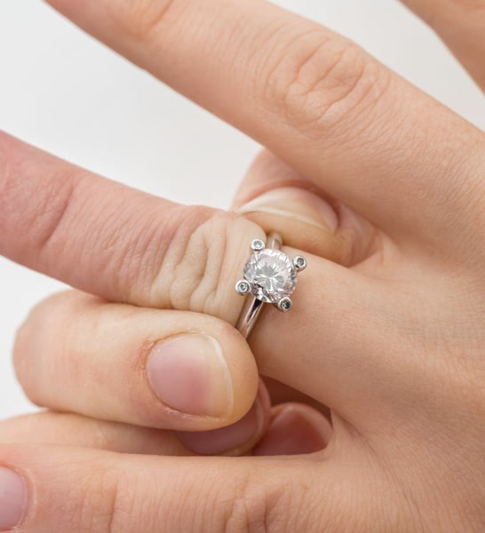 A woman tries to remove her engagement ring, but it is not the right size and too tight to slide over her knuckle.