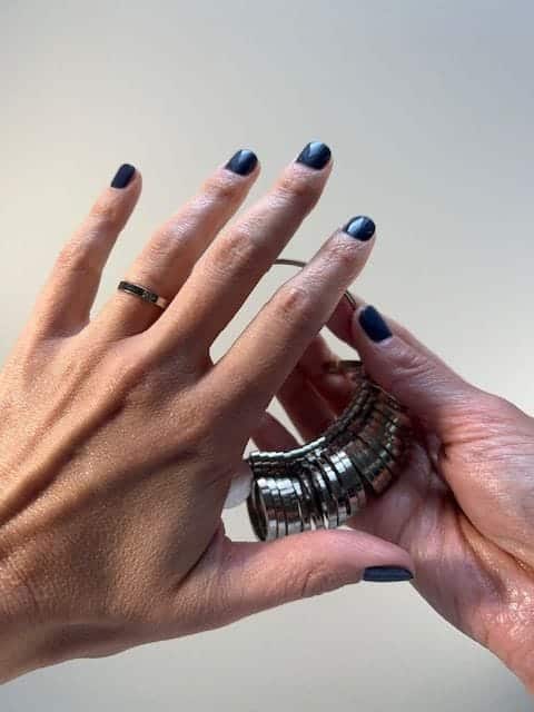 A woman slips a metal ring from a ring sizer onto her ring finger.