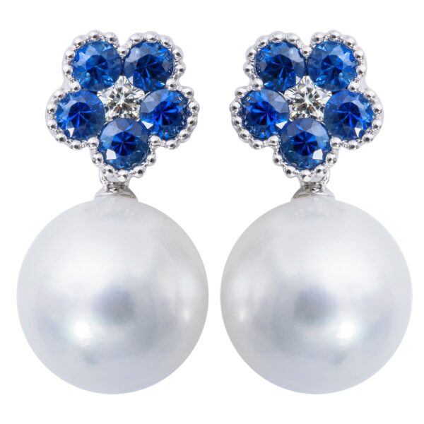A pair of 18 karat white gold drop earrings featuring a blue sapphire and diamond flower blossom that drops down to a white South Sea Pearl