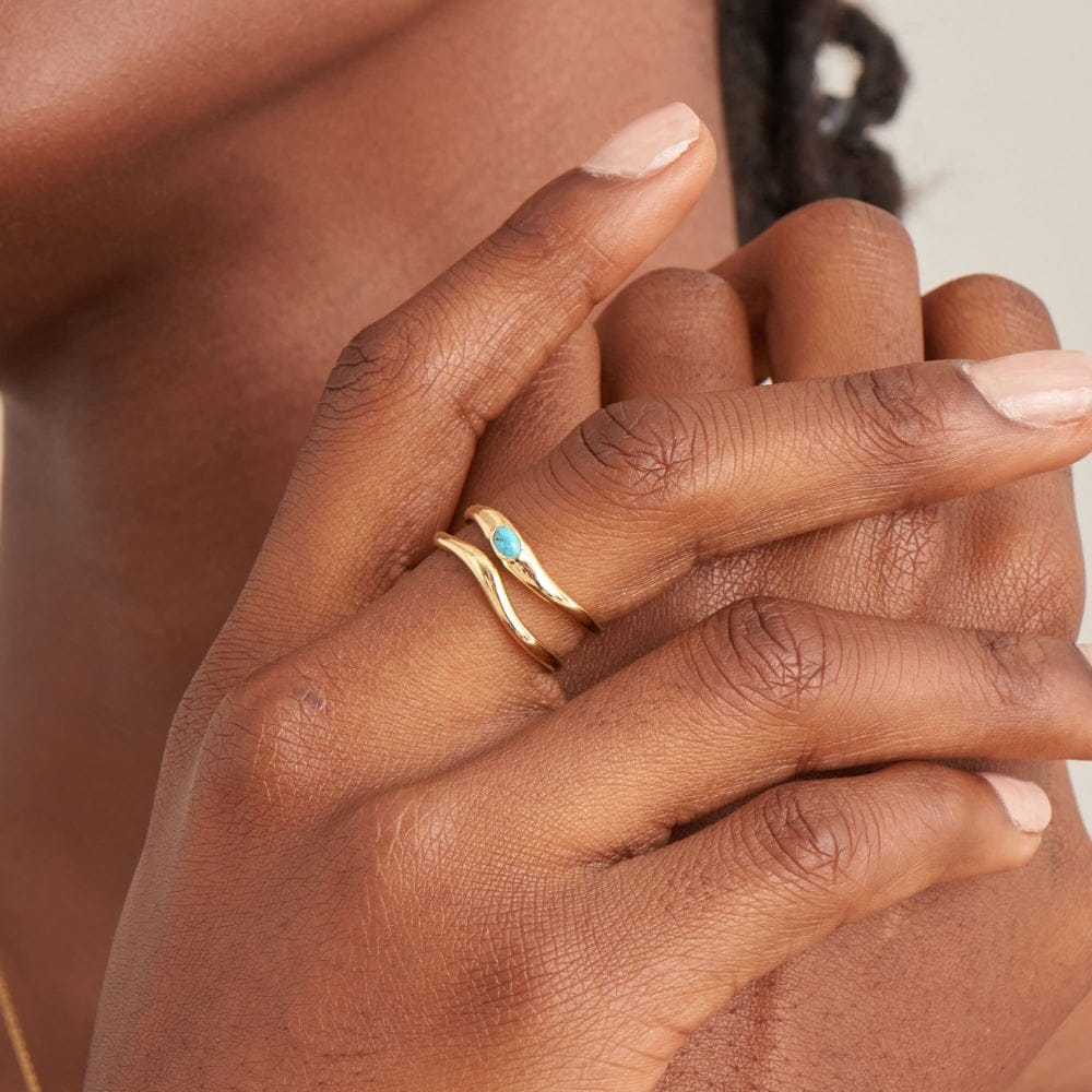 A model wearing a yellow gold-plated double band with a wave-style design and a single synthetic turquoise