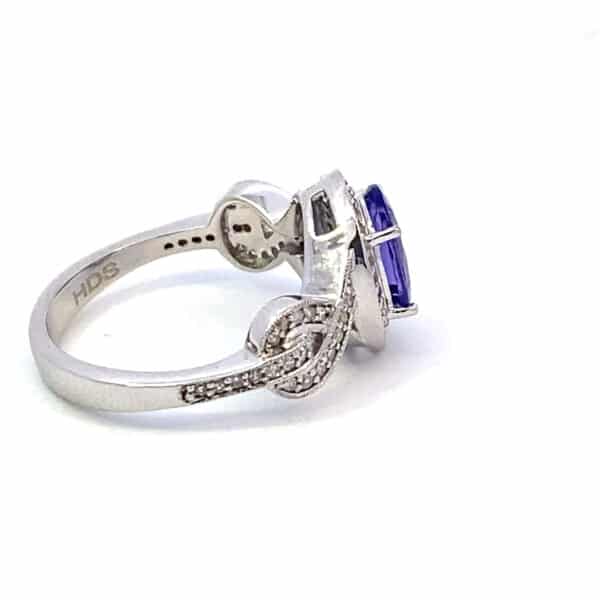 A 14 karat white gold ring by Lali with a center oval faceted tanzanite measuring 9x7mm and round diamonds set in the halo and in a partial figure-eight twist design in the band