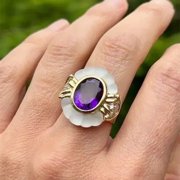 An estate 14 karat yellow gold fashion ring featuring an oval amethyst with scalloped glass to the north and south and diamonds set to the east and west