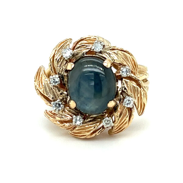 An estate 14 karat yellow gold halo ring with a center oval cabochon blue sapphire and gold wreath-inspired halo with diamond accents
