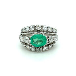 An estate vintage platinum three-row ring featuring an oval emerald and three rows of round diamonds