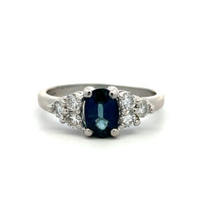 An estate platinum ring with an oval blue sapphire and clusters of diamonds on either side