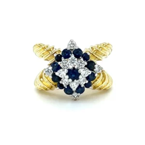 an estate 18 karat two-tone gold ring featuring a white gold head set with blue sapphires and diamonds and a yellow gold split shank textured band