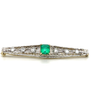 An estate antique Art Deco bar pin made from 14 karat two-tone gold with a center emerald and diamond and filigree accents