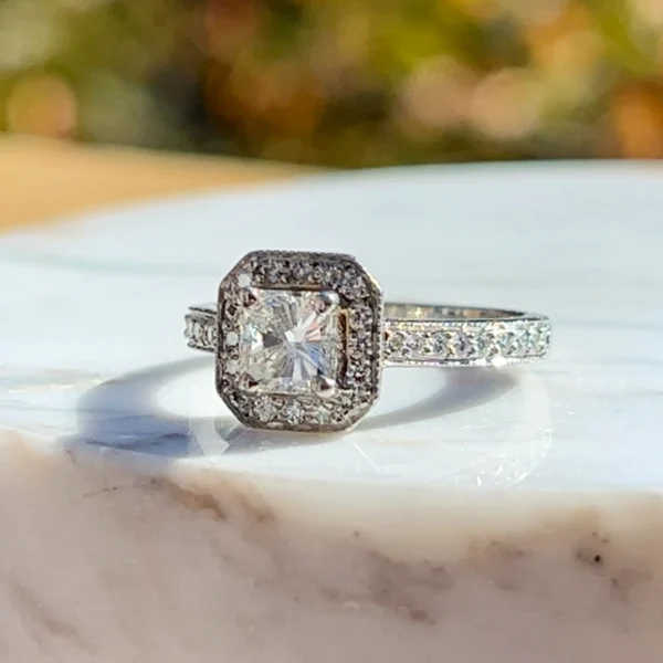 One estate plantium halo engagement ring with a center radiant-cut diamond weighing 0.75 carat and 24 round brilliant accent diamonds weighing 0.28 carat total weight set in the halo and in the band