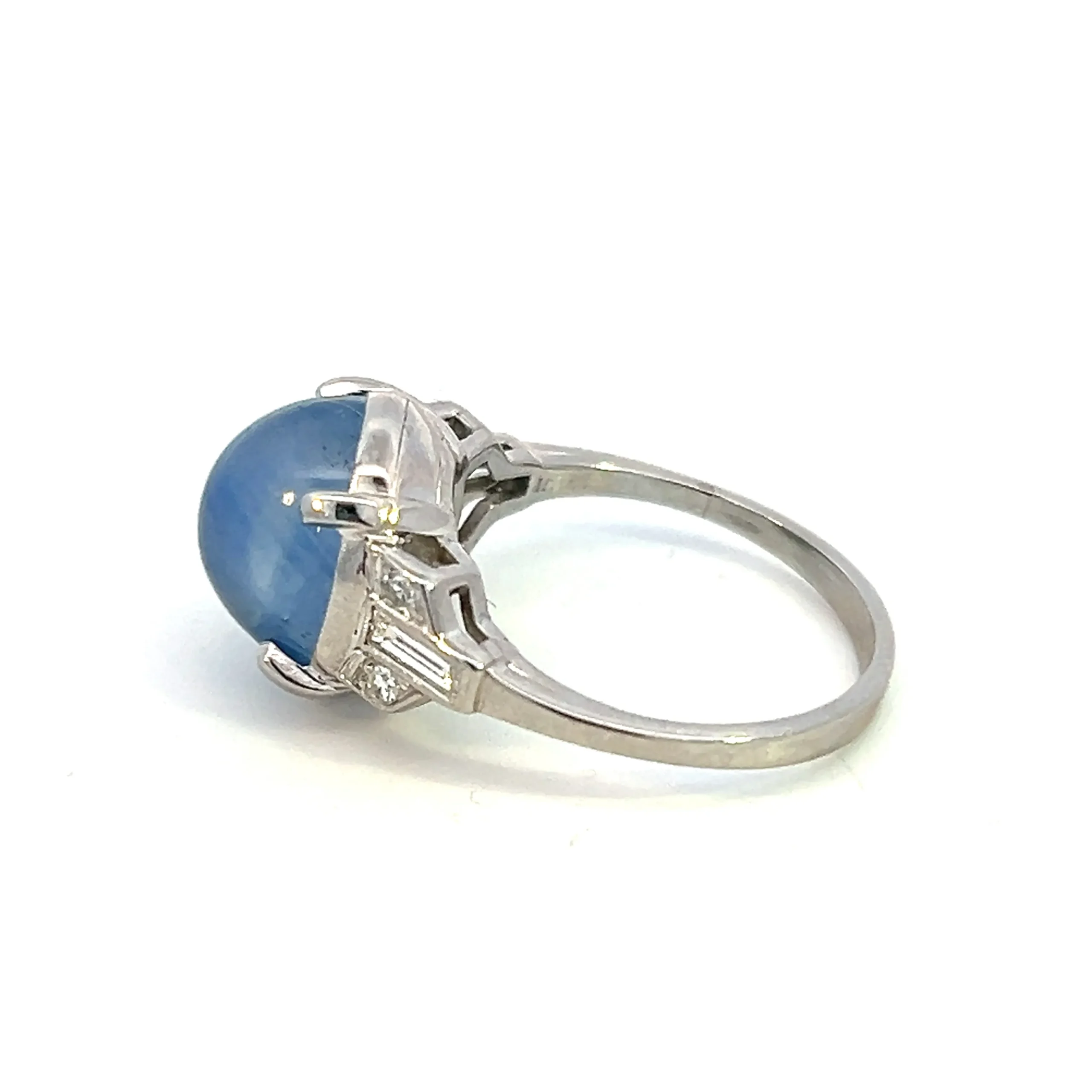 estate platinum ring set with 1 oval cabochon cornflower blur star sapphire weighing 9.62 carats accented on the shoulders with 4 single cut diamonds weighing 0.08 total carat weight and 2 baguette cut diamonds weighing 0.24 total carat weight. The ring is vintage from the 1920s.