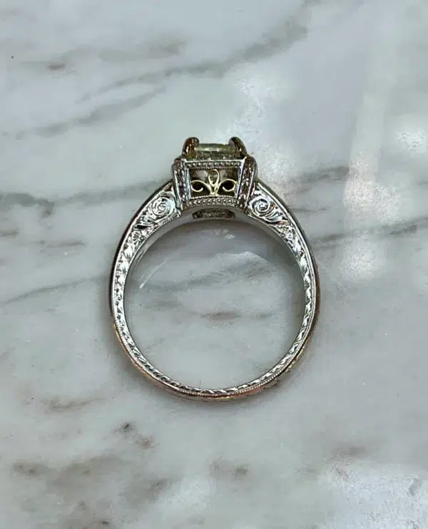 One estate platinum halo engagement ring by Michael Beaudry with a center radiant-cut diamond weighing 1.01 carats and 24 round brilliant diamonds set in the halo and in the band. The under carriage has an 18 karat yellow gold filigree accent