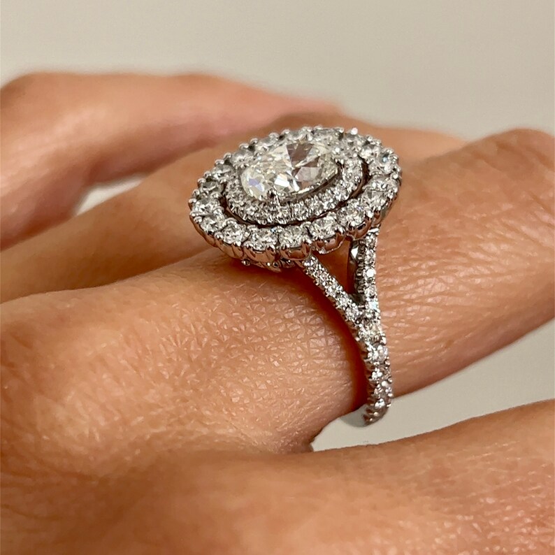 One estate 18 karat white gold double halo engagement ring with a center oval diamond weighing 1.51 carats and 40 round brilliant diamonds set in 2 oval-shaped halos and 34 round brilliant diamonds in the split-shank band