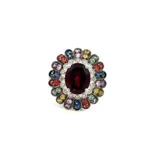 One estate sterling silver floral design cluster ring with a center oval garnet measuring 10x8mm surrounded by a halo of 16 round brilliant diamonds in bezel settings surrounded by an outer halo of 36 round multi-color round stones in hues of yellow, pink, green, red, and blue. The outer halo features 2 stones of the same color in an oval-shaped setting creating a petal-inspired motif.