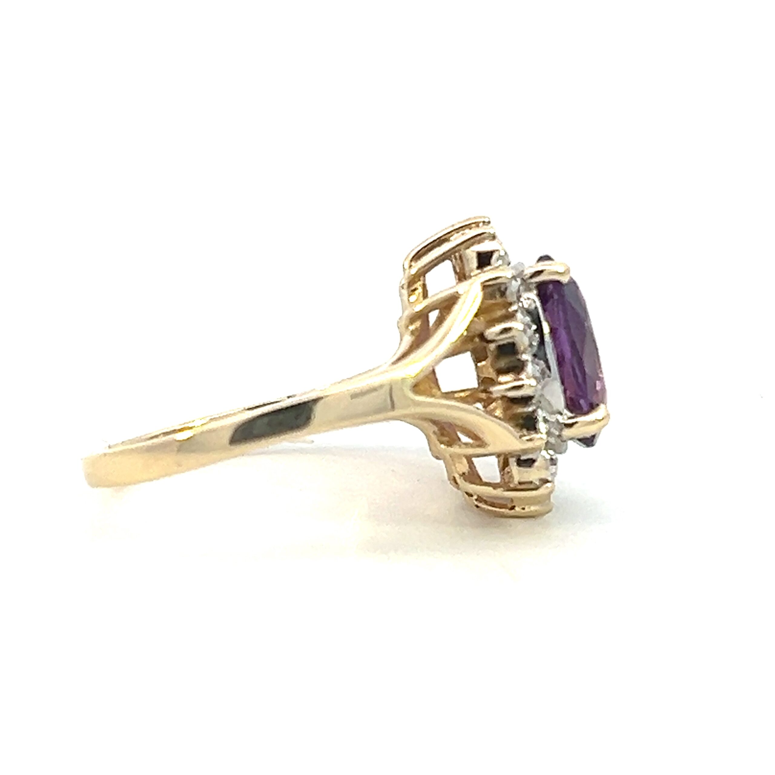 One estate 14 karat yellow and white gold amethyst and diamond halo ring containing an oval amethyst measuring 10x8mm and containing 14 round brilliant diamonds in a scalloped halo. The ring is primarily crafted from yellow gold with the diamond set in white gold. The shoulders feature a split-shank design. Vintage from the 1970s.