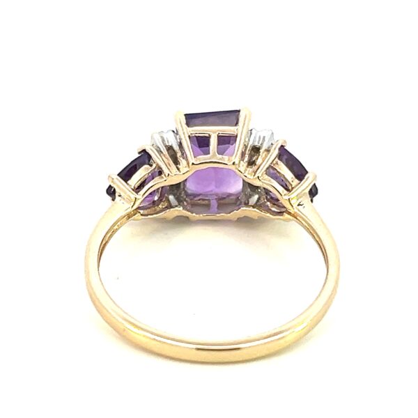 One estate vintage 10 karat yellow and white gold amethyst and diamond ring containing a center emerald-cut amethyst measuring 8x6mm and 2 trillion-cut amethyst measuring 5mm each. In between the center amethyst and each side amethyst are 3 round brilliant diamonds with all 6 diamonds weighing 0.06 carat total weight in white gold settings with the remainder of the ring being yellow gold. The ring is vintage from the 1970s.